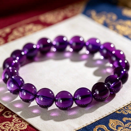 Flat lay shot of high clarity natural amethyst beaded bracelet on ornate Tibetan patterned fabric, healing quartz accessory