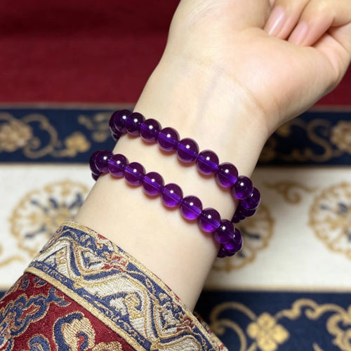 Natural polished purple amethyst quartz bracelet worn on wrist with traditional Tibetan embroidered sleeve, spiritual gemstone jewelry