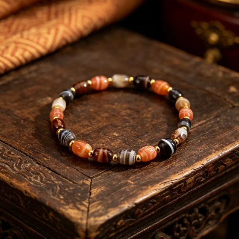 Purely handcrafted Tibetan banded agate bracelet with natural silk agate barrel beads and gold accents, held in a palm.