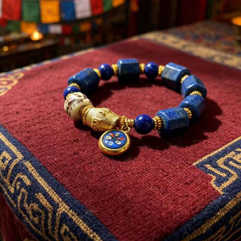 Lapis lazuli beaded bracelet laid flat showing a yak bone skull bead and Black Jambhala wealth charm with Tibetan prayer flags in the background