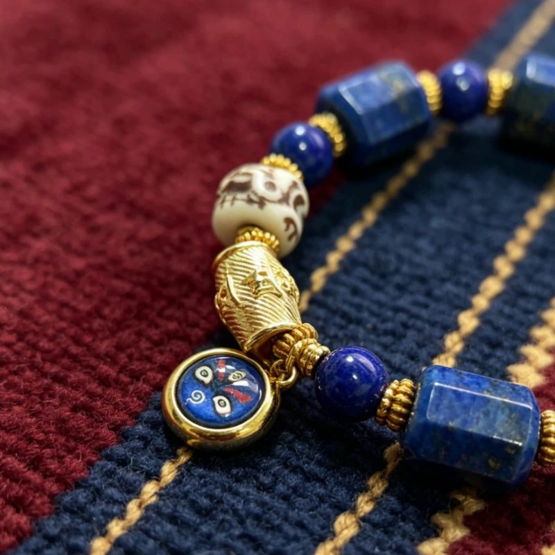 Close-up of lapis lazuli bracelet detail featuring a Black Jambhala enamel charm, carved yak bone skull bead, and gold accents