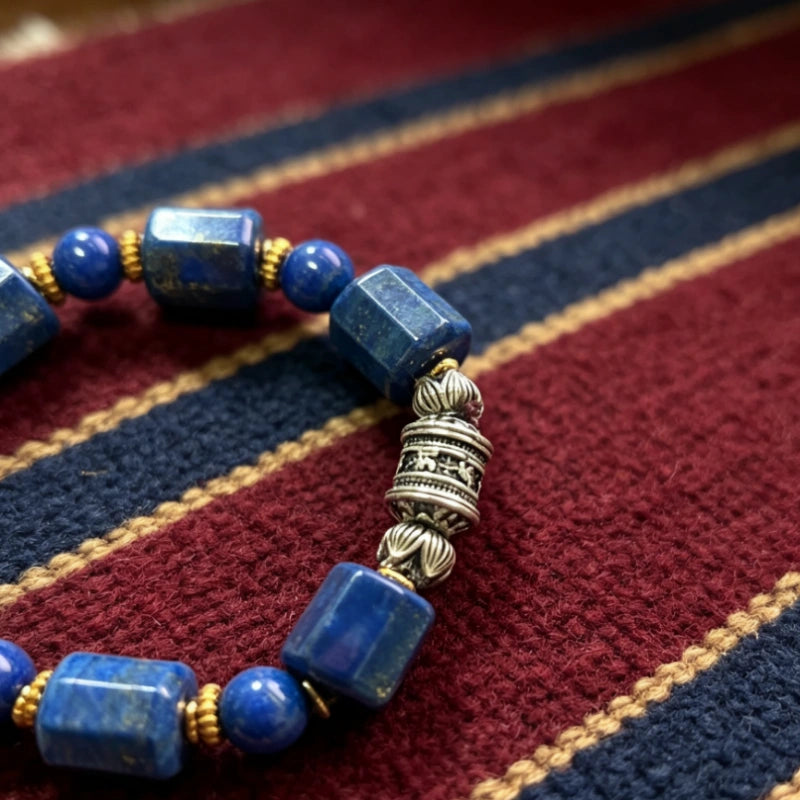 Natural lapis lazuli bracelet featuring a hand-carved Tibetan silver prayer wheel bead with lotus end caps