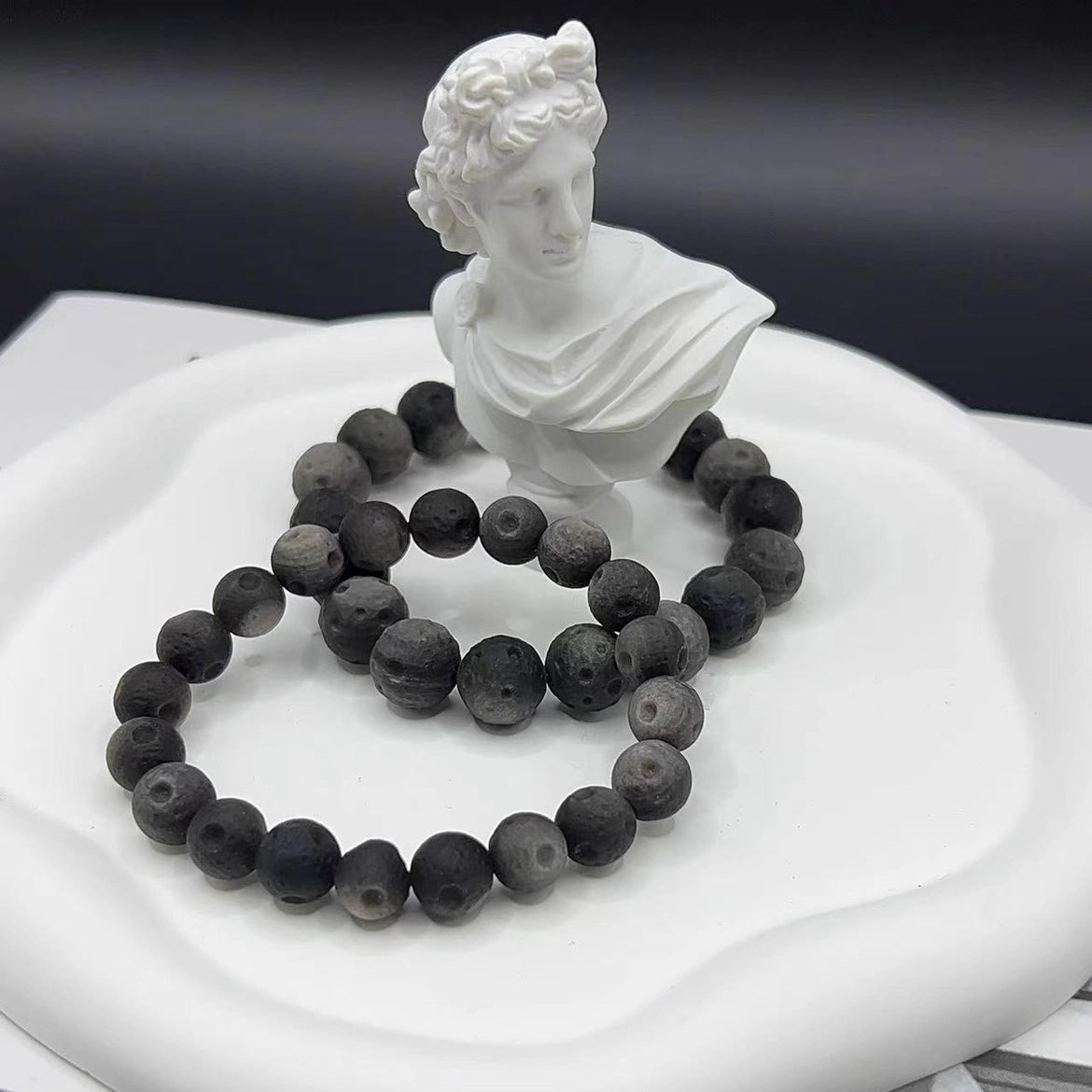 Obsidian meteorite design crystal bracelet placed beside decorative statue, portable energy protection stone jewelry for stress relief