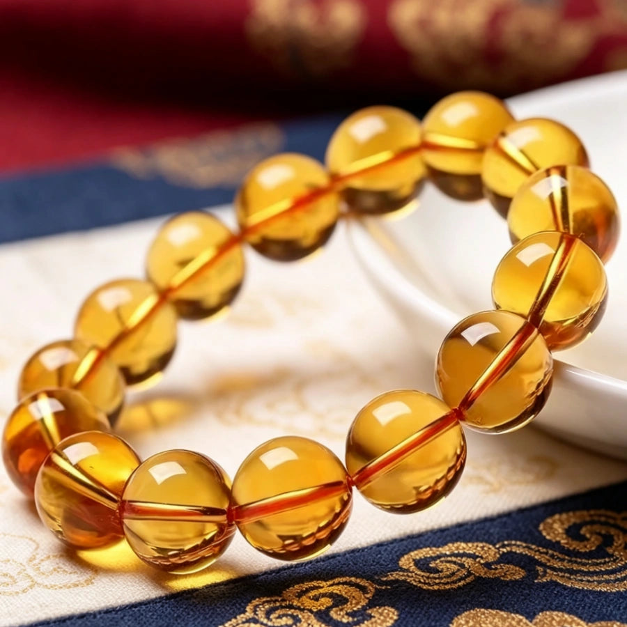 Natural polished citrine bead bracelet displayed beside white porcelain dish, translucent golden quartz on ornate Tibetan brocade