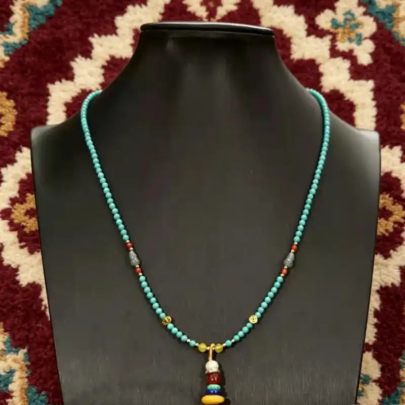 Turquoise tassel necklace displayed on a stand, showing its full collarbone length and centered charm pendant